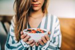 Crop woman close up eating oat and fruits bowl for breakfast