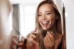 Photo of an amazing beautiful young woman in lingerie underwear looking at mirror apply her lipstick lip gloss doing makeup.