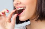 Portrait of the beautiful smiling, girl eating chocolate cookies isolated on gray background.